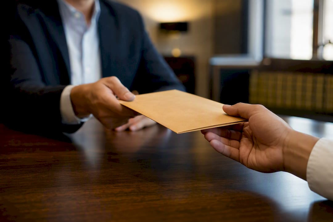 Hands exchanging sealed envelope in law office
